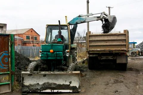 An old Soviet tractor digs and loads waste stone processing near the shop Stock Photos