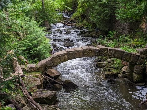 Old stone archway going over a flowing stream in a forest during summer Foto stock