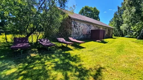 Old stone barn and empty sun loungers by a tranquil pond on a sunny day Stock Footage 343977982