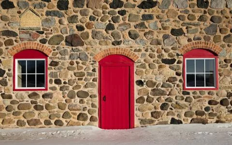 Old stone barn with bright red door and two windows Stock Photos
