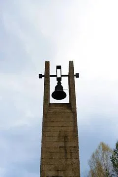 Old stone bell tower with bell on cloudy sky background Stock Photos