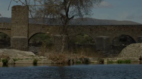 Old stone bridge with multiple arches crossing a tranquil river Stock Footage 335461687
