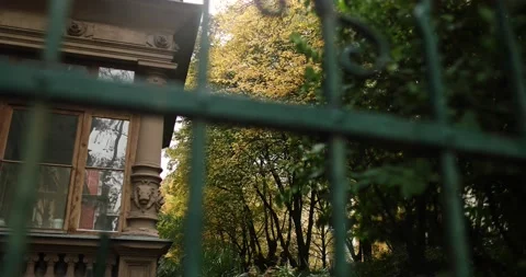 Old stone building guarded by green iron fence with autumn trees in background Stock Footage 230487366