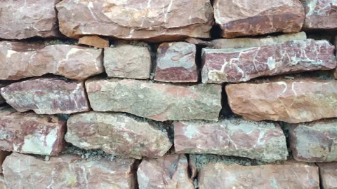 Old stone retaining wall made of irregularly laid blocks of red and pink rock. Stock Footage 233145238