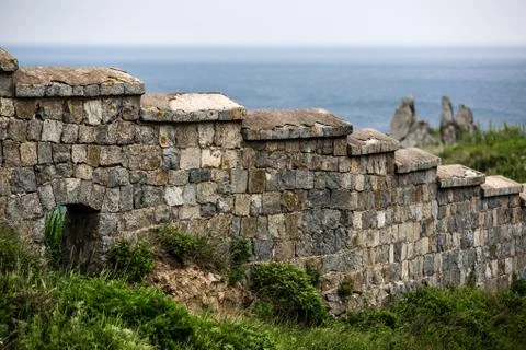 Old stone wall on the background of rocks and the sea Stock Photos