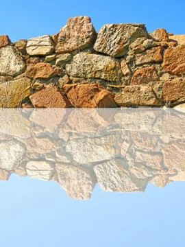 Old stone wall being reflected in water. Stock Photos