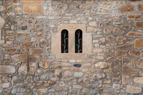 Old stone wall with a double arched window and metal grating Stock Photos