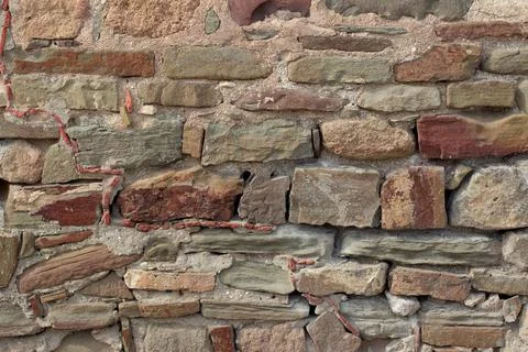 Old stone wall made of various square natural stones in beige, ocher, red and Stock Photos