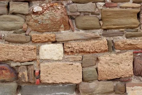 Old stone wall made of various square natural stones in beige, ocher, red and Stock Photos