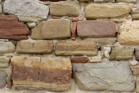 Old stone wall made of various square natural stones in beige, ocher, red and Stock Photos