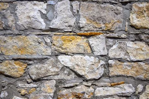 An old stone wall texture. Grey color stones with yellow tint. Stock Photos