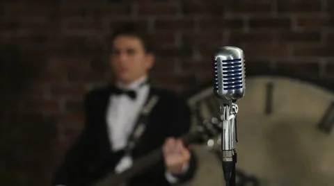 Old style microphone stand on front. Man plays the guitar on the background Stock Footage 65254353