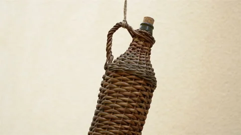 An old, stylish, wicker wine bottle hanging on a rope in front of a wine cellar. Stock Footage 106634744
