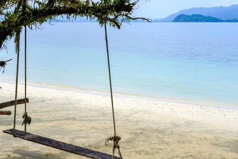Old swing hanging on a tree on sandy beach, blue sea and sky background. Stock-Fotos