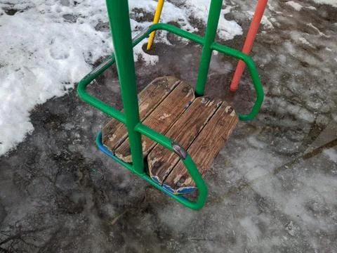 Old swing in the yard against the background of melted snow 스톡 사진