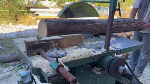Old table circular saw in open area processing big bark-covered log, operator Stock Footage 326038132