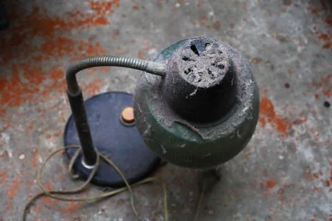 Old table lamp under a large layer of dust stands on a concrete floor, focus Stock Photos