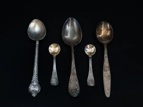 Old tea spoons of different sizes lie on a black background Stock Photos