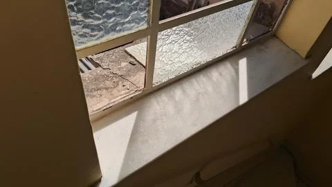 Old textured window glass casting sharp shadows on white sill Stock Photos