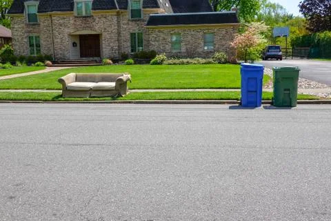 An old torn couch seen on the curb in front of a big house Stock Photos