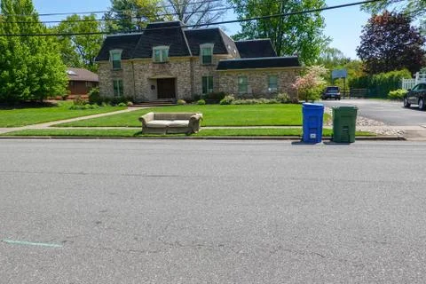 An old torn couch seen on the curb in front of a big house Stock Photos