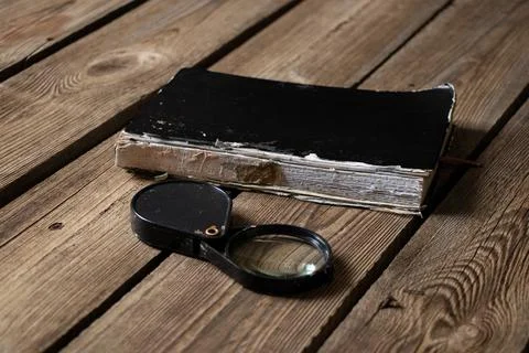 An old torn notebook and a magnifying glass lie on a wooden table Stock Photos