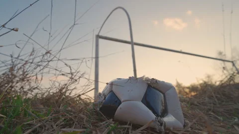 Old Torn Soccer Ball Lying in Dry Grass Behind Abandoned Goal | Decline Concept Stock Footage 345621831