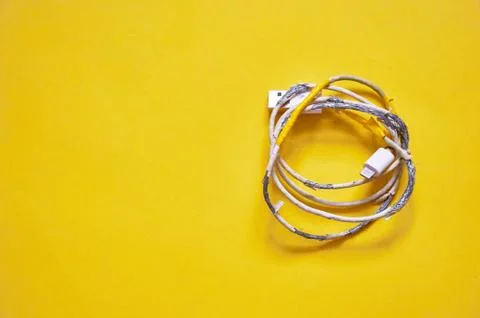 An old torn USB cord is lying on a yellow background. The view from the top. Stock Photos