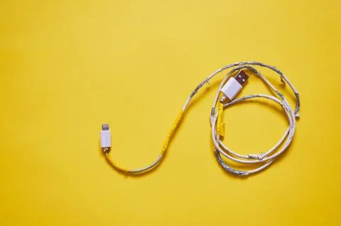 An old torn USB cord is lying on a yellow background. The view from the top. Stock Photos