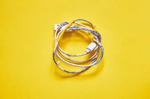 An old torn USB cord is lying on a yellow background. The view from the top. Stock Photos