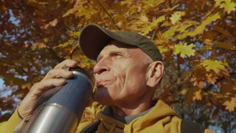 Old tourist with backpack drinks hot tea or coffee from thermo cup Video stock 164364158