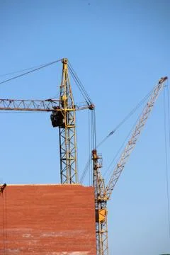 Old tower cranes raise brick blocks against a blue sky Stock Photos