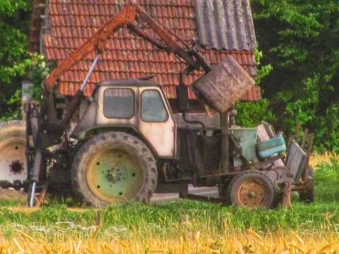 Old tractor with a bucket loader attachment parked in a farm yard Stock Photos