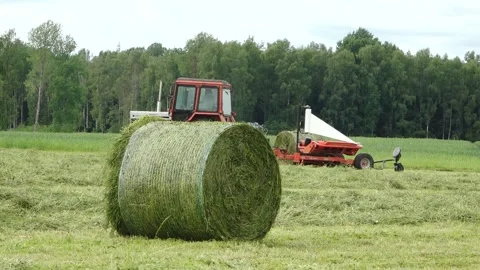 Old tractor pulls a bale wrapper across a cut grass field Video stock 337256890
