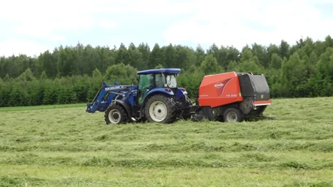 Old tractor pulls a bale wrapper across a cut grass field Video stock 337256895