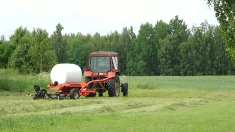 Old tractor pulls a bale wrapper across a cut grass field Video stock 337256935