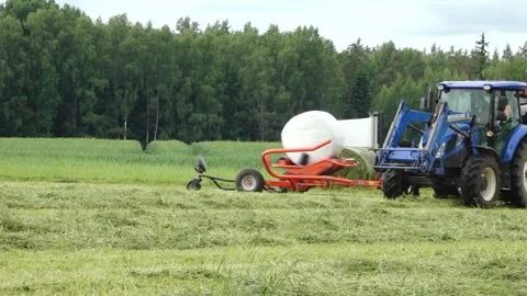 Old tractor pulls a bale wrapper across a cut grass field Video stock 337256961