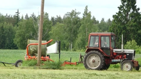 Old tractor pulls a bale wrapper across a cut grass field Video stock 337257063