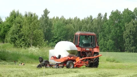 Old tractor pulls a bale wrapper across a cut grass field Video stock 337257124
