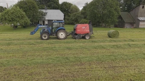 Old tractor pulls a bale wrapper across a cut grass field Video stock 337257337