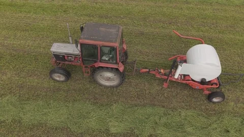 Old tractor pulls a bale wrapper across a cut grass field Video stock 337741541