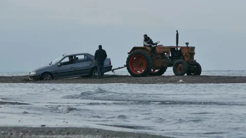 Old tractor rescuing stranded car on beach as waves roll in Stock Footage 320744614