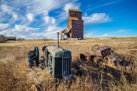 An old tractor is sitting in a field next to a grain elevator Stock Photos