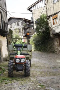 Old tractor on the street next to Typical houses with granite stone plinths.. Stock Photos