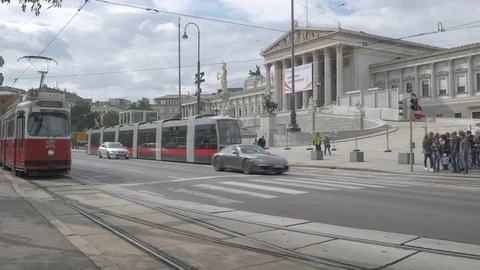 Old tram pulls away from stop in front of Austrian parliament building in Vienna Stock Footage 82426723