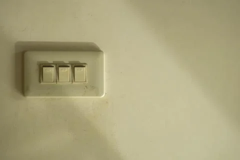 Old triple light switch on a beige textured wall with shadows 스톡 사진