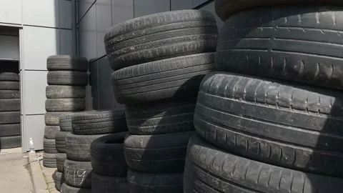 Old used summer and winter tires stand against a gray wall piled on top of each  Stock Footage 130791406