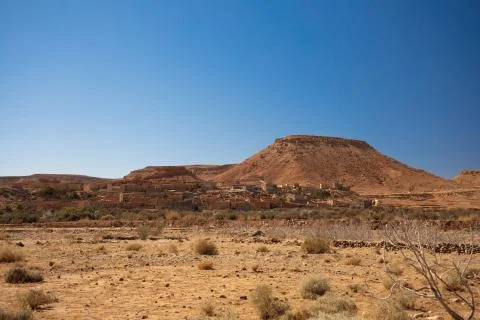 Old village hidden on the desert valley between hills on blue sky background Stock Photos