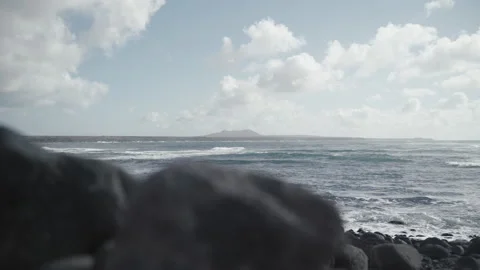 Old volcano in the distance, stone beach with sea waves, cloudy and windy day Stock Footage 235677975