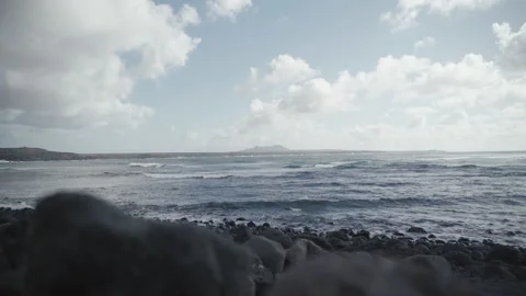Old volcano in the distance, stone beach with sea waves, cloudy and windy day Stock Footage 235678310